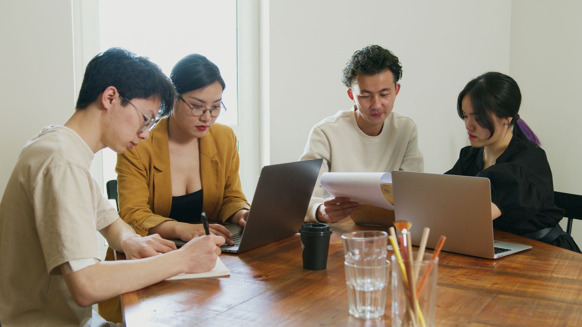 Ein kleines Team arbeitet an einem Holztisch mit Laptops und Unterlagen.